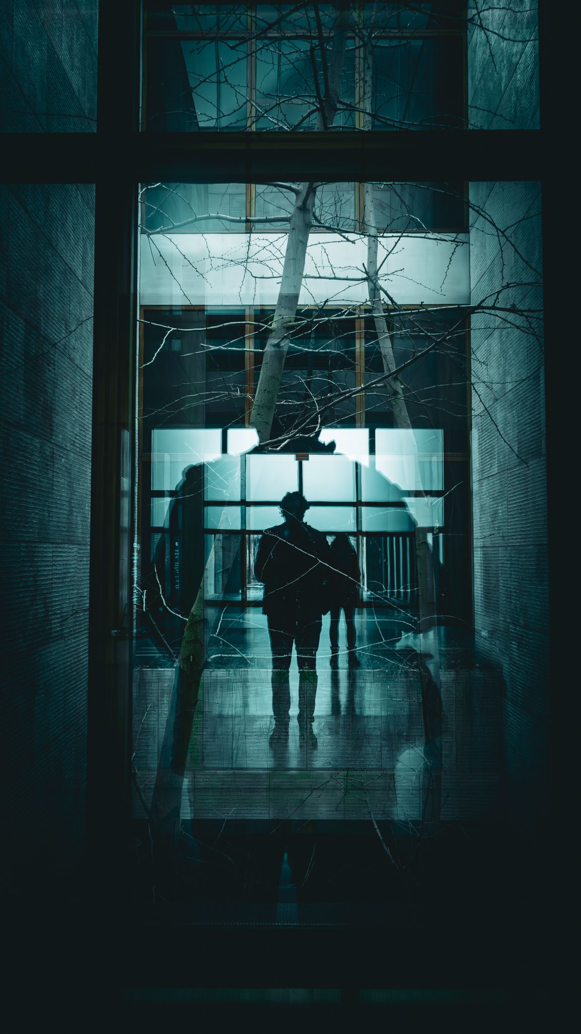 Silhouetted figures stand in a dark, eerie corridor with teal lighting creating a haunting atmosphere.