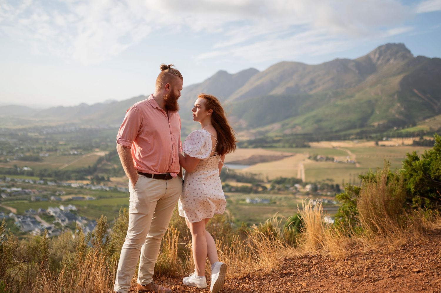 A couple walks along a scenic mountain trail during golden hour in a beautiful countryside setting.