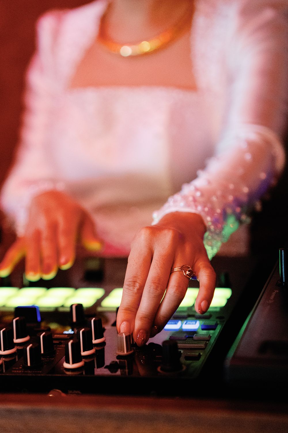 Close-up of bride's hands with wedding ring operating a DJ mixer at reception.
