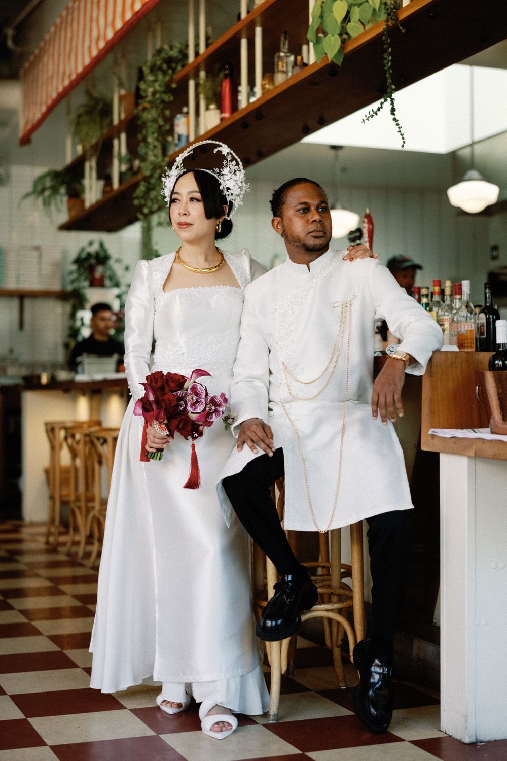 Interracial couple in matching white traditional wedding attire posing together inside a vintage restaurant.