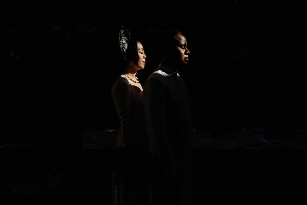 Dramatic silhouette portrait of a couple standing back to back in dark moody lighting.