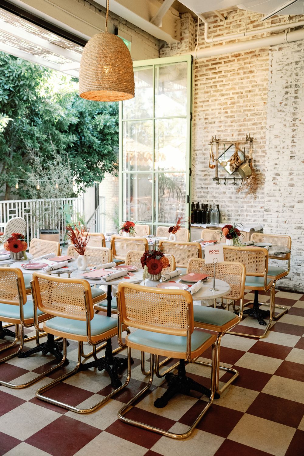 Elegant wedding reception dining setup with cane chairs on checkered floors and exposed brick walls.