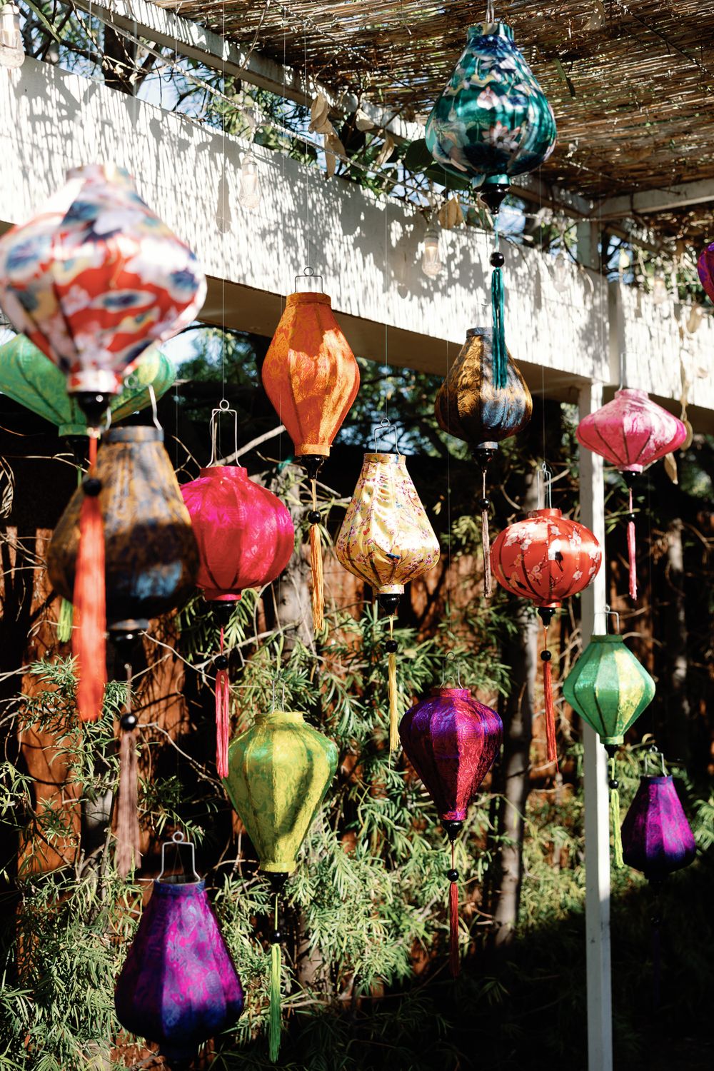 Colorful silk lanterns hanging outdoors in sunlight creating a festive garden display.