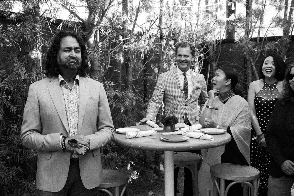 Black and white photo of wedding guests laughing together outdoors around a cocktail table.