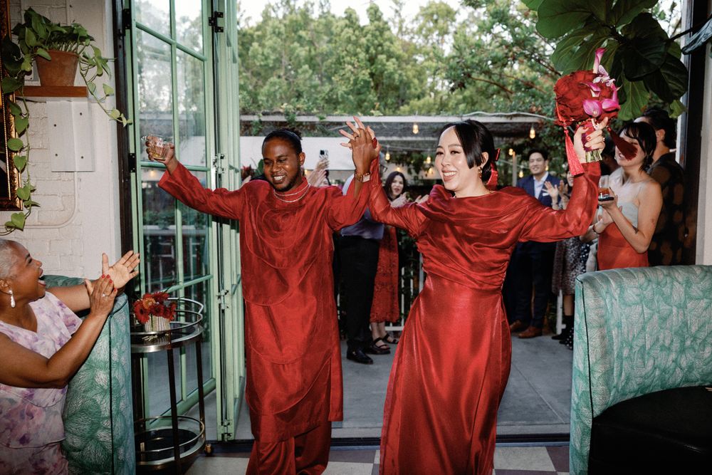 Couple making grand entrance in matching red traditional Vietnamese ao dai outfits at wedding reception.
