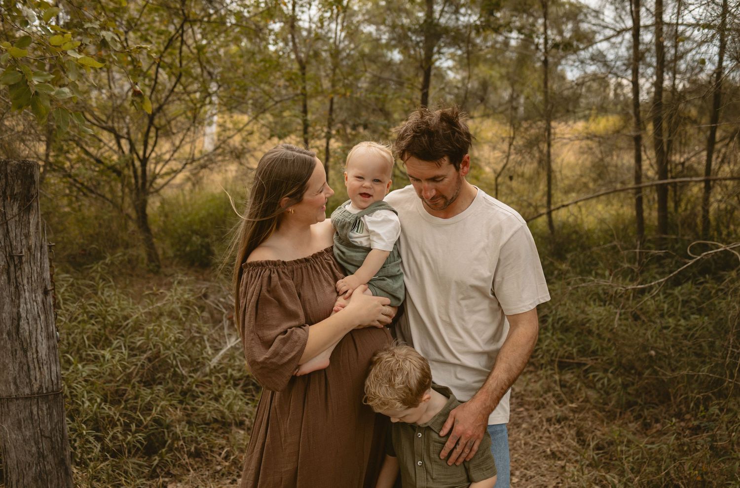 Romantic couple and toddler share tender moments in a golden-lit forest setting during autumn.
