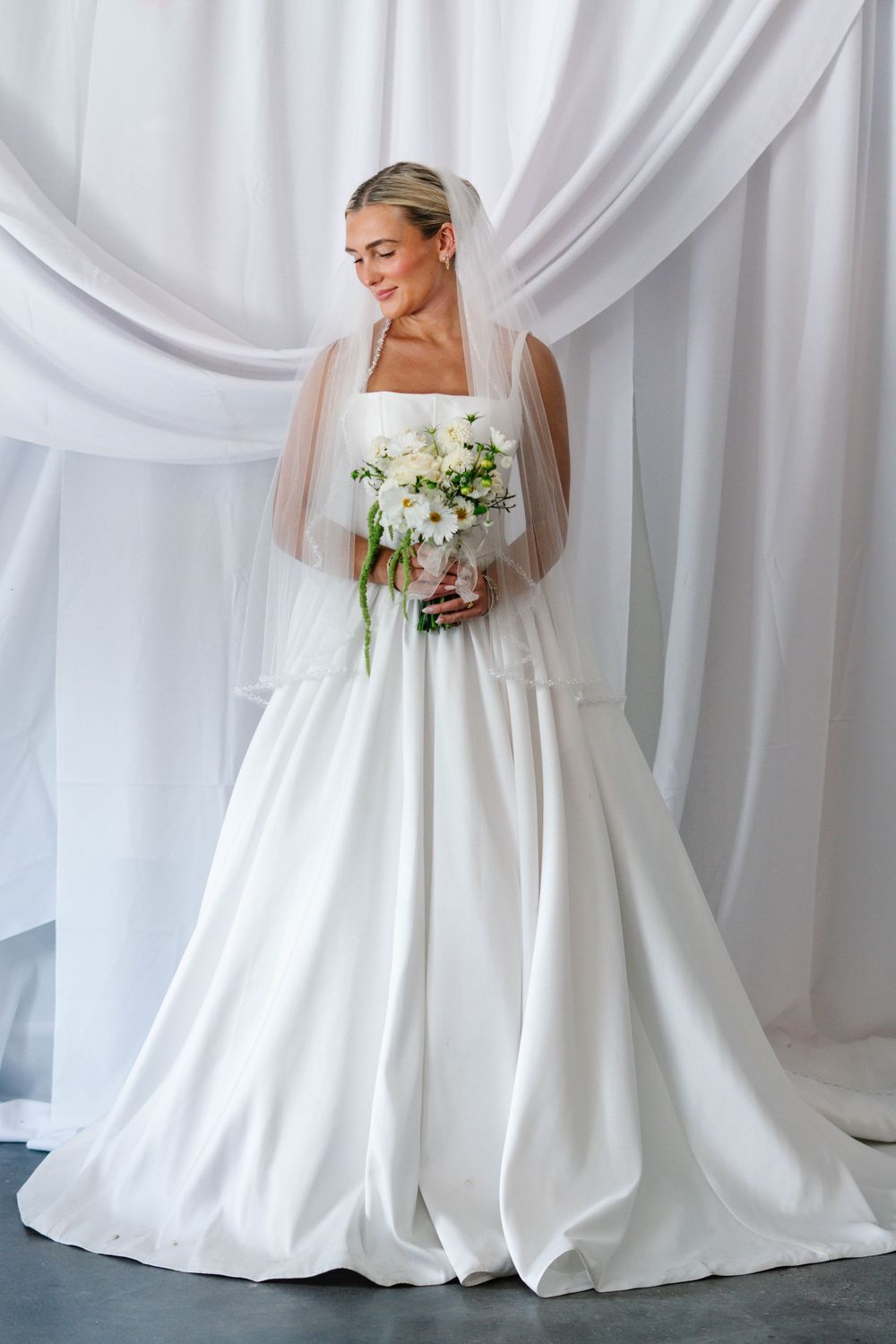 Elegant bridal portraits with flowing white gown against draped fabric backdrop.