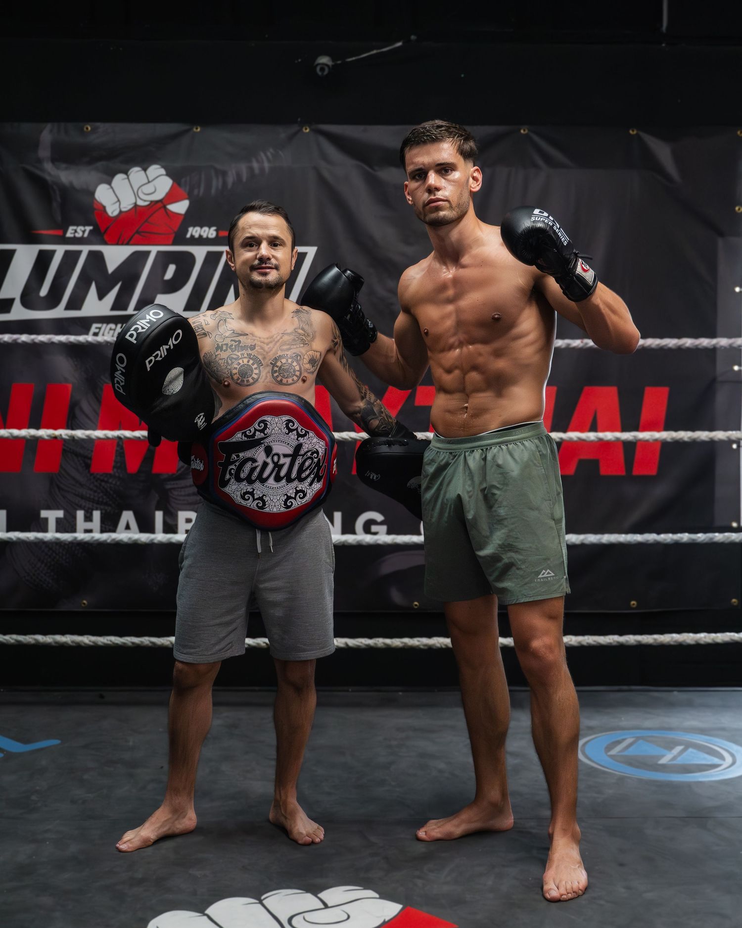 Mixed martial arts athletes standing in fighting stance on a black mat with promotional banners.