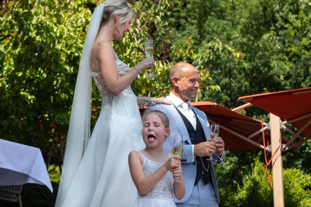 Bruidspaar met hun dochter tijdens de receptie bij L Seven, haar reactie na een slok champagne
