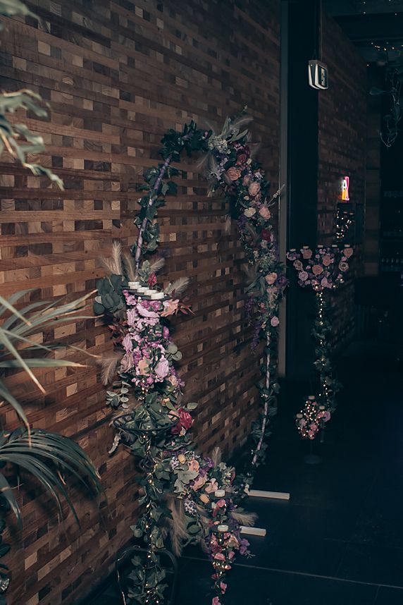 Pink cherry blossoms cascade down a dark brick wall in a moody interior setting.