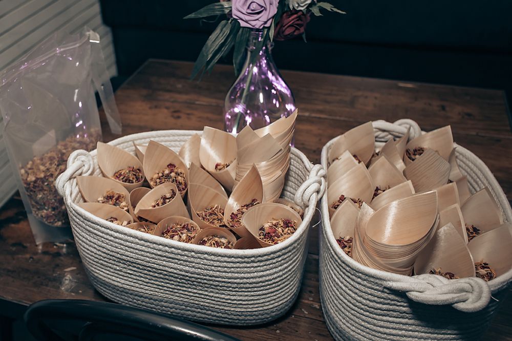 Wedding reception place settings with delicate folded napkins and elegant purple floral centerpieces on wooden tables.
