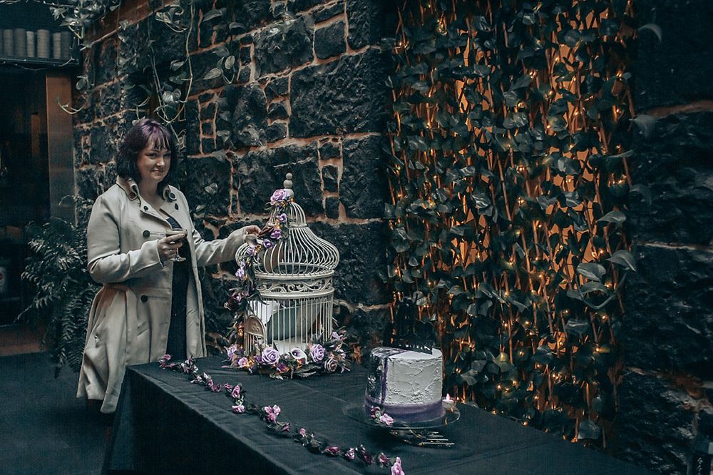 A silver vintage style birdcage sits on a stand with flowers against a backdrop of orange autumn leaves.