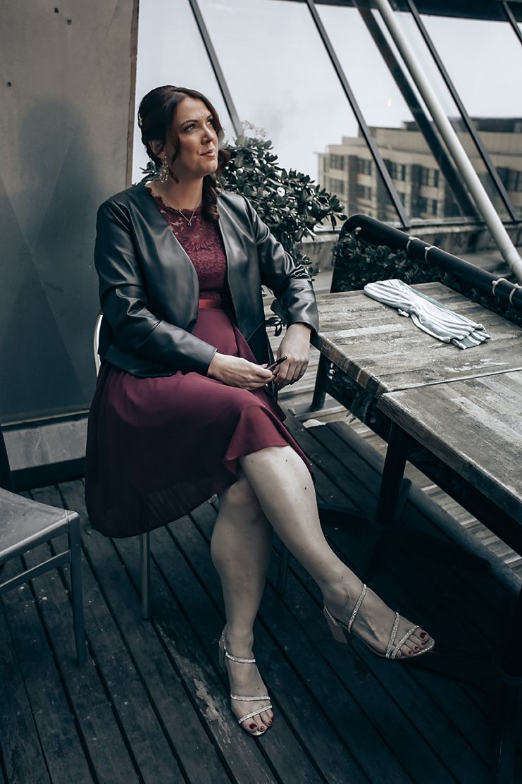 Person in a dark jacket and burgundy dress relaxing on a deck during an overcast day.
