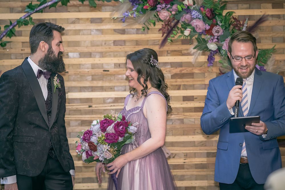 Wedding celebration at rustic venue with wood paneling and purple floral decorations.