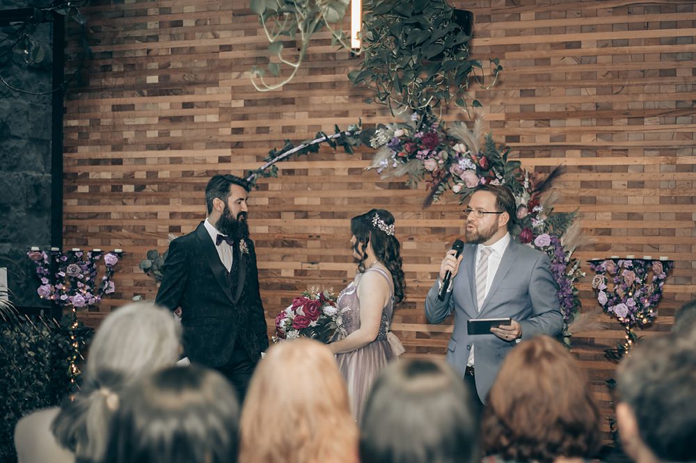 Wedding ceremony taking place in front of exposed brick wall with floral arrangements inside a church.