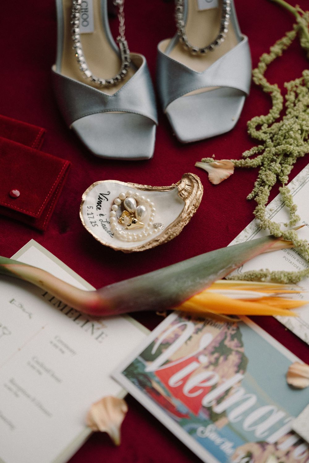 Elegant wedding accessories including silver high heels, pearls, and a magazine arranged on a deep red velvet surface.