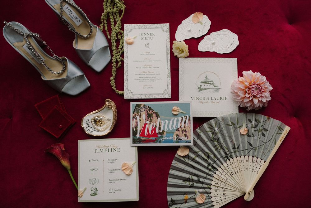Pink and burgundy wedding stationery details with folding fan and floral accents elegantly arranged on dark background.