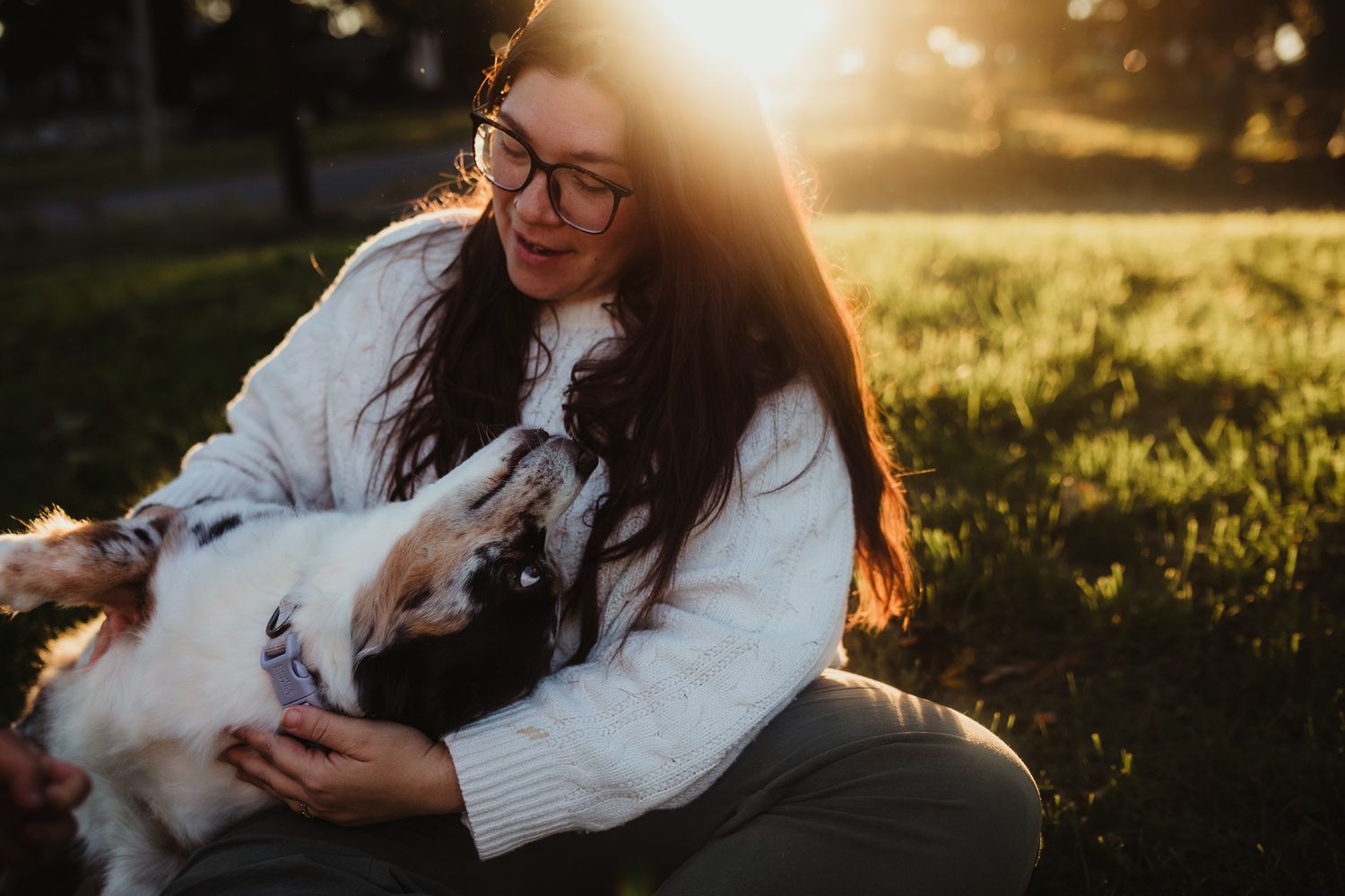 A person in white holding a small pet during golden hour.
