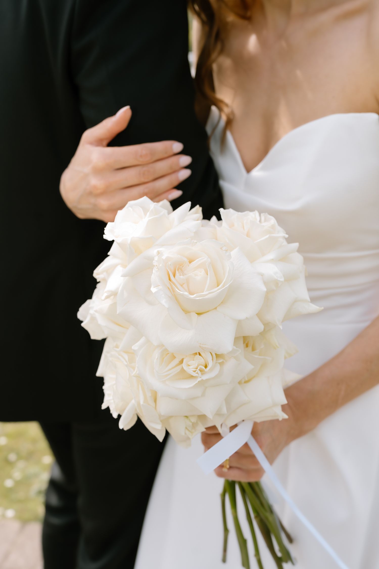 A classic white rose wedding bouquet held against a bride's white dress.
