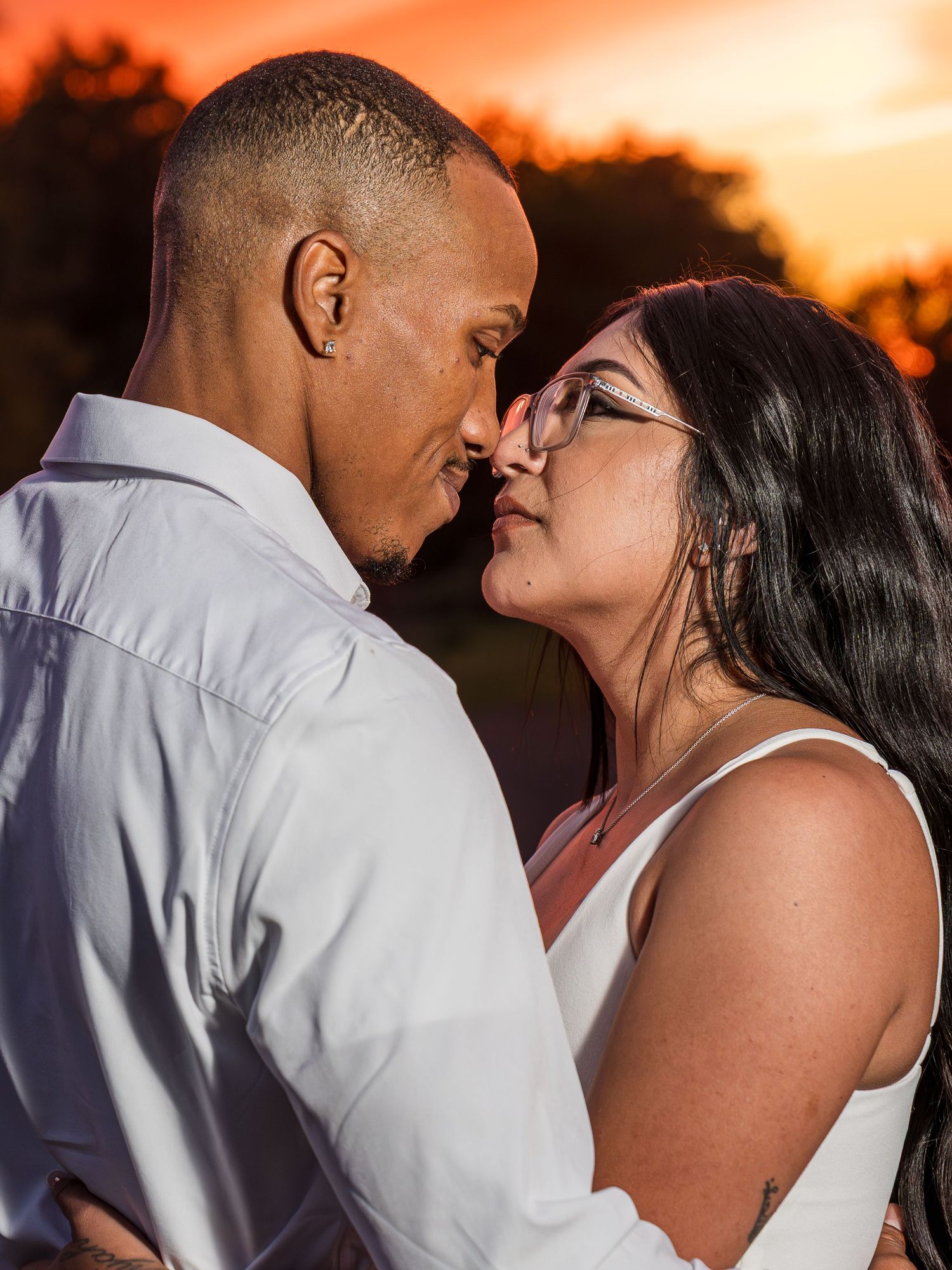 A couple shares an intimate moment during sunset, creating a romantic silhouette against an orange sky.