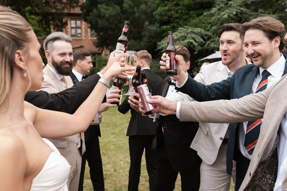 Wedding guests in formal attire toast and raise their drinks in celebration at an outdoor garden reception.