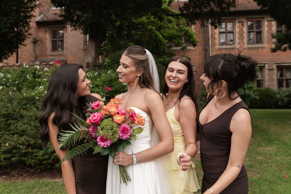 Friends share laughter and hugs in a garden courtyard during a summer celebration with pink floral bouquets.