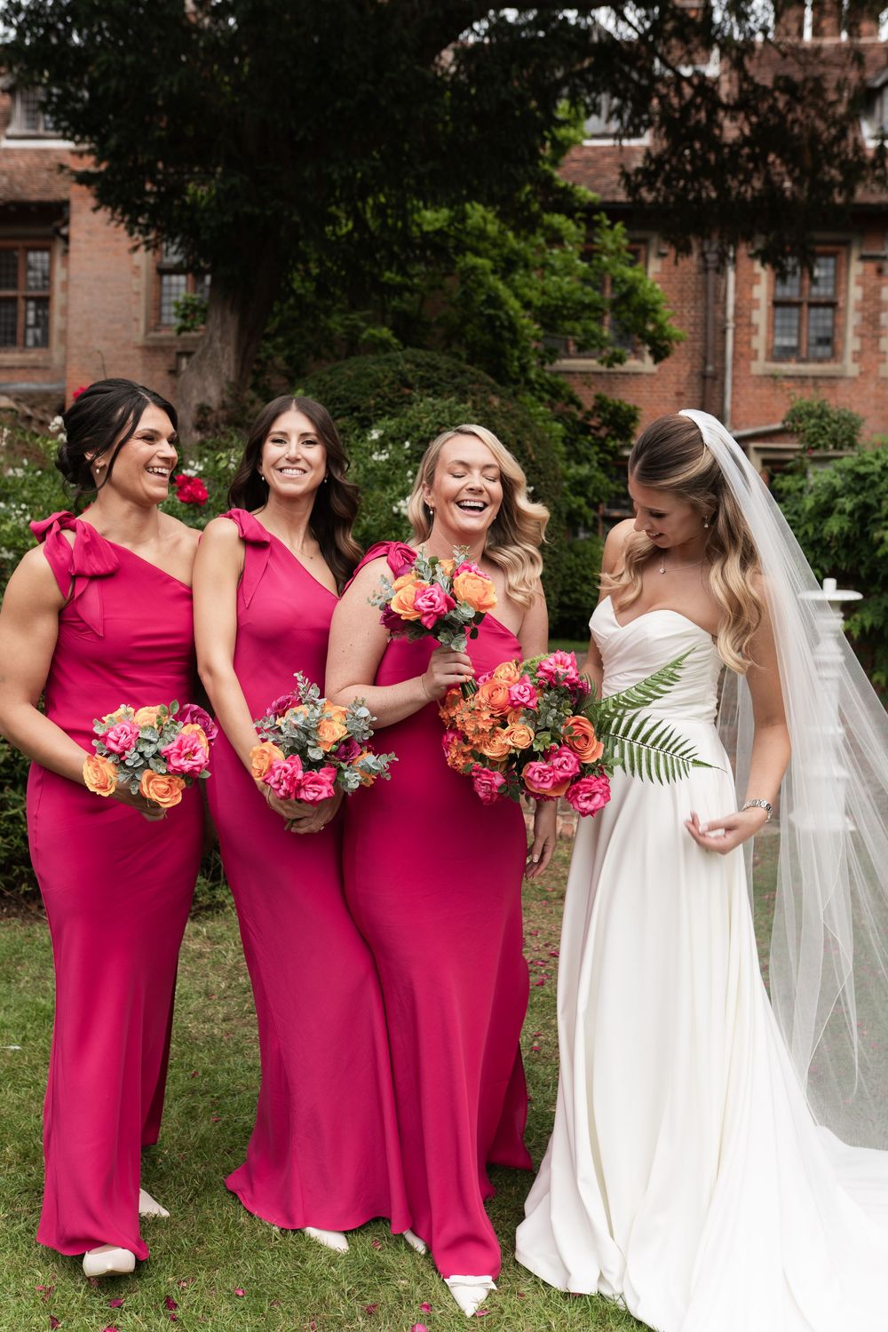 Bridal party in vibrant pink dresses and a bride in white pose together during an outdoor wedding photoshoot.
