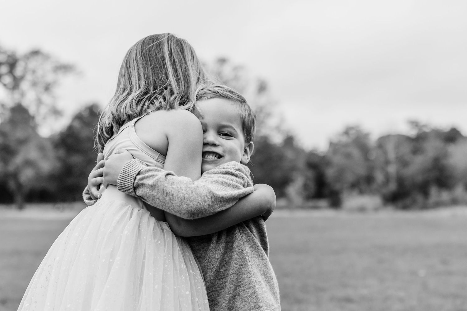 Black and white image of people embracing in a field with trees in the background.
