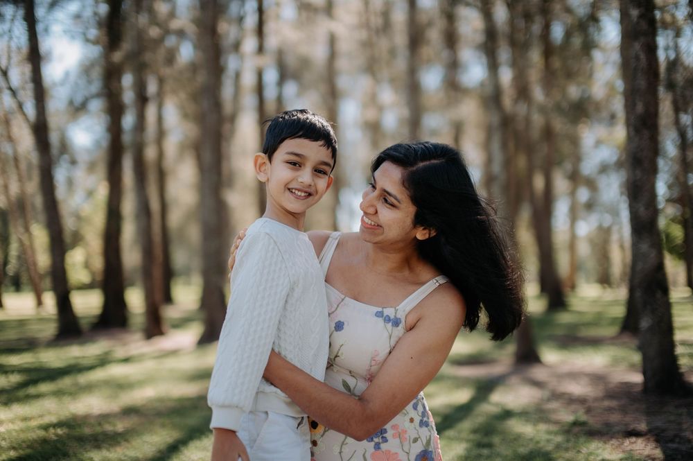 A mother and son share a loving embrace while standing in a sunlit forest on a bright spring day.