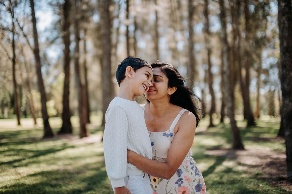 Couple embracing in a sunlit forest with tall trees creating a romantic natural backdrop.