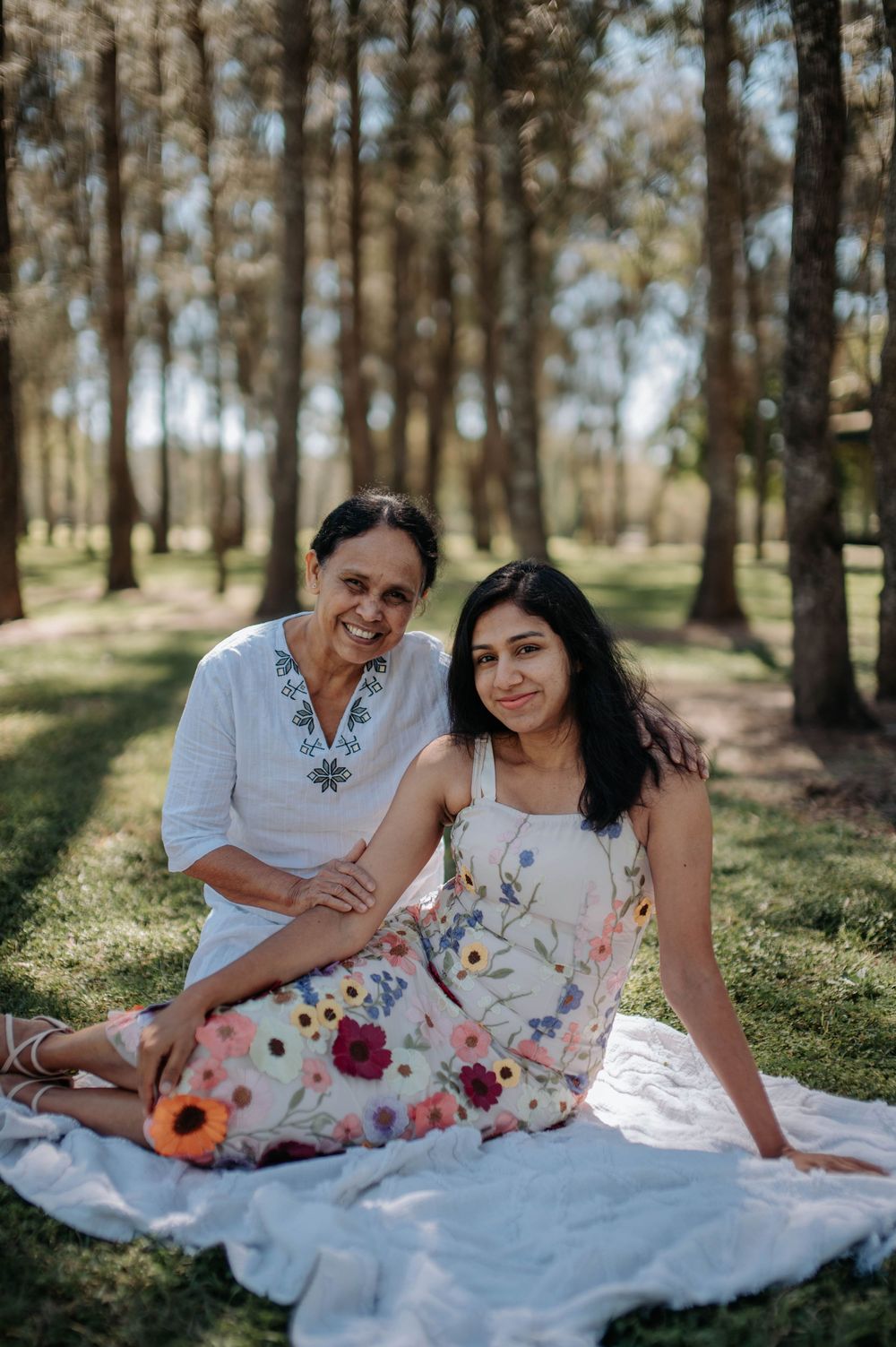 Two people in white outfits having a picnic under trees in a sunny forest setting.