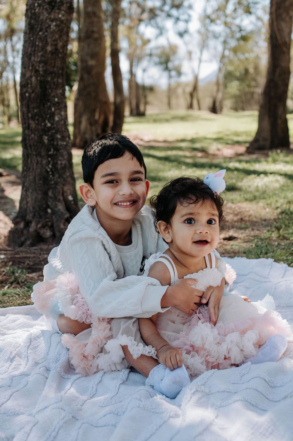 Children in white tulle dresses playing and posing together on the ground outdoors.