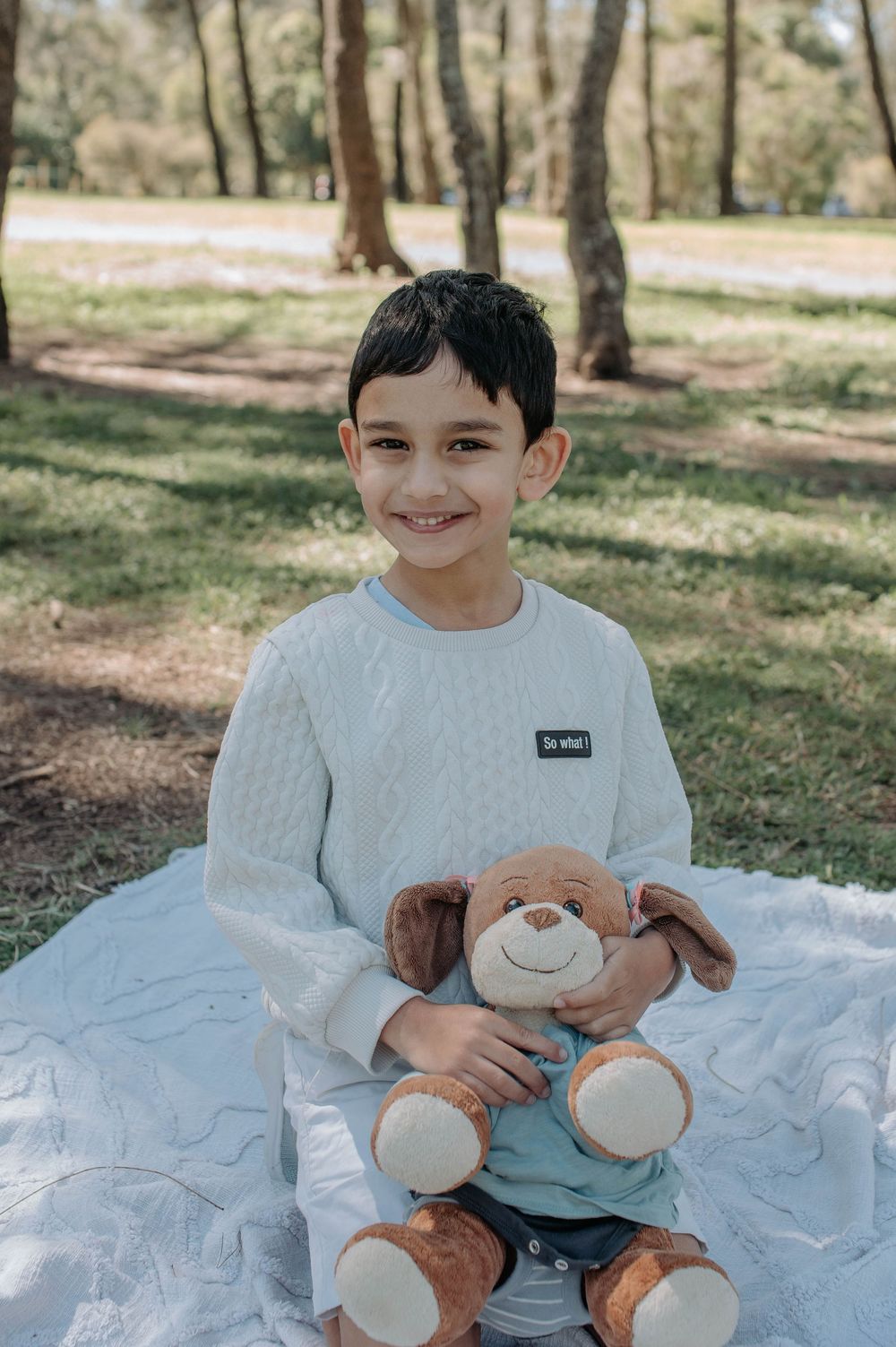 A series of photos showing a child in white clothing holding a brown teddy bear plush toy in an outdoor setting.