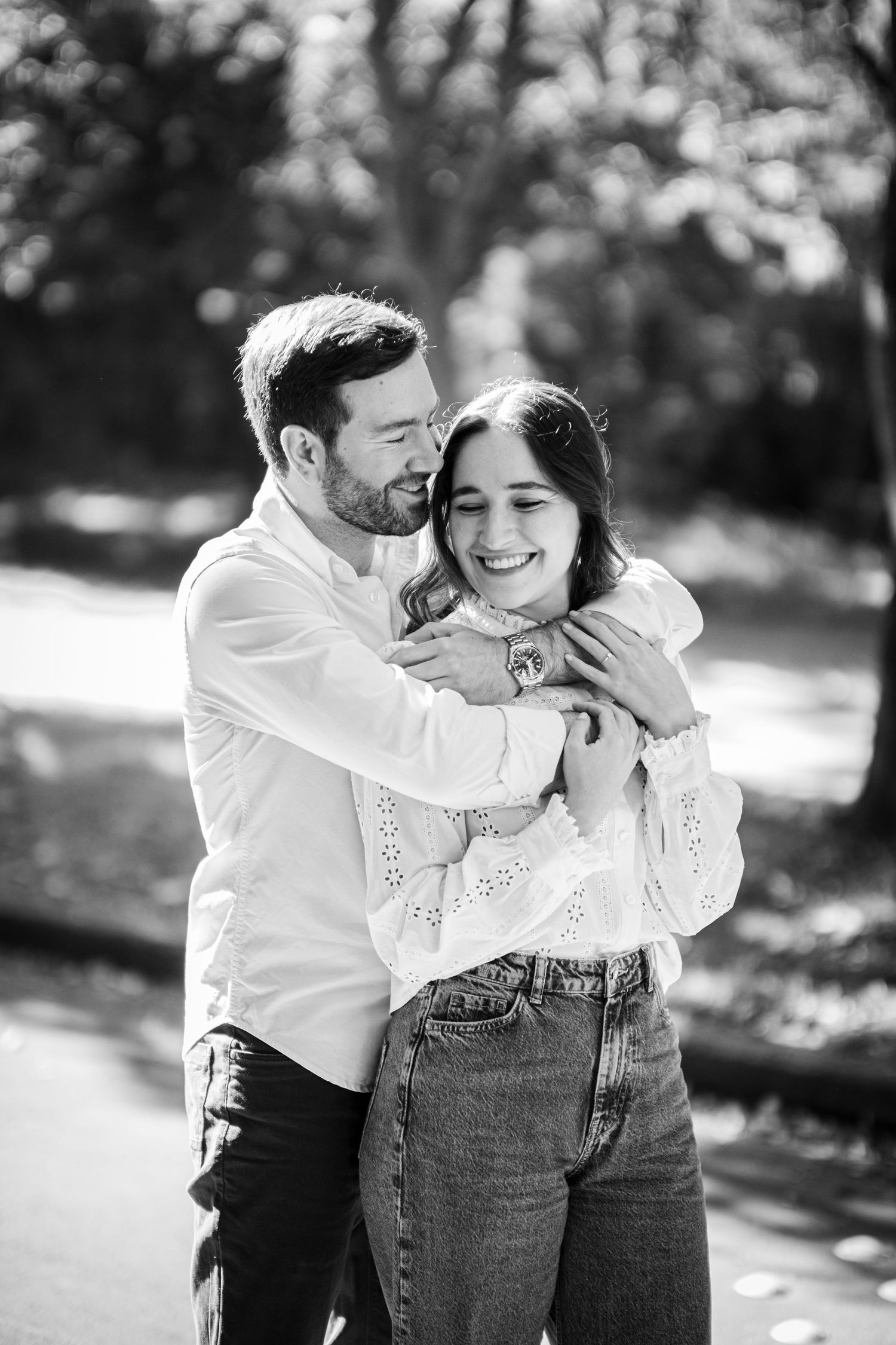 A happy couple walking and laughing together in casual white outfits along a sunlit outdoor path.