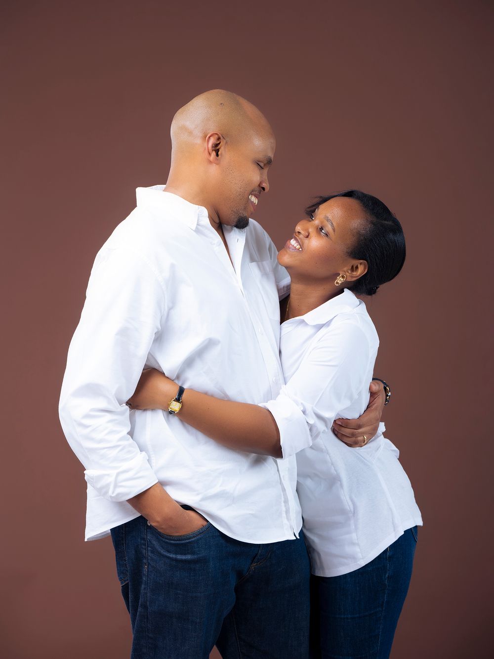 Couple in matching white shirts and jeans share intimate moments against a brown backdrop.