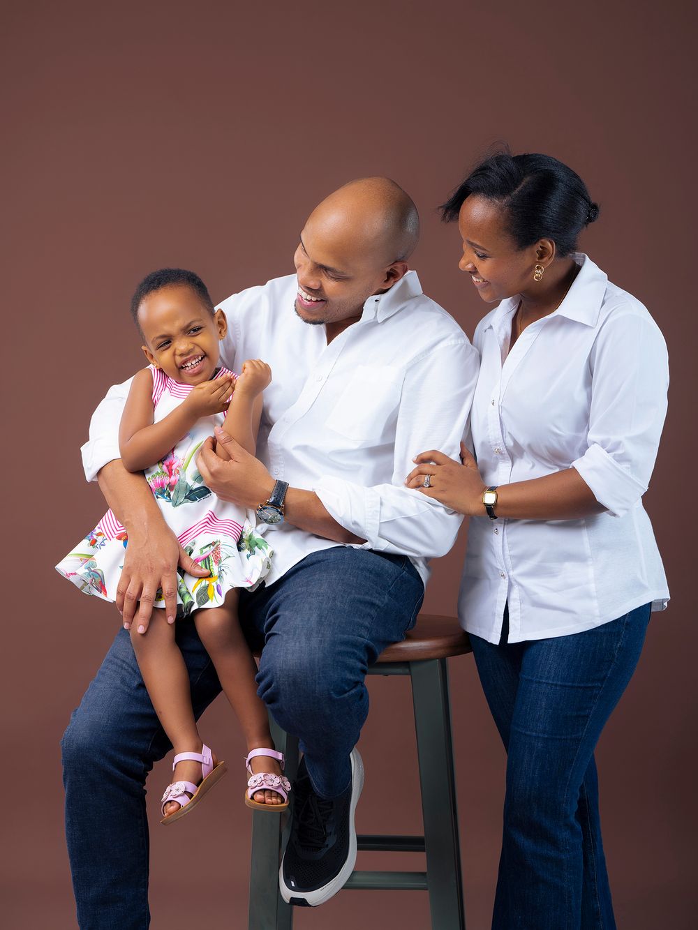 A joyful sequence of family members playing and laughing together in coordinated white shirts and jeans against brown backdrop.