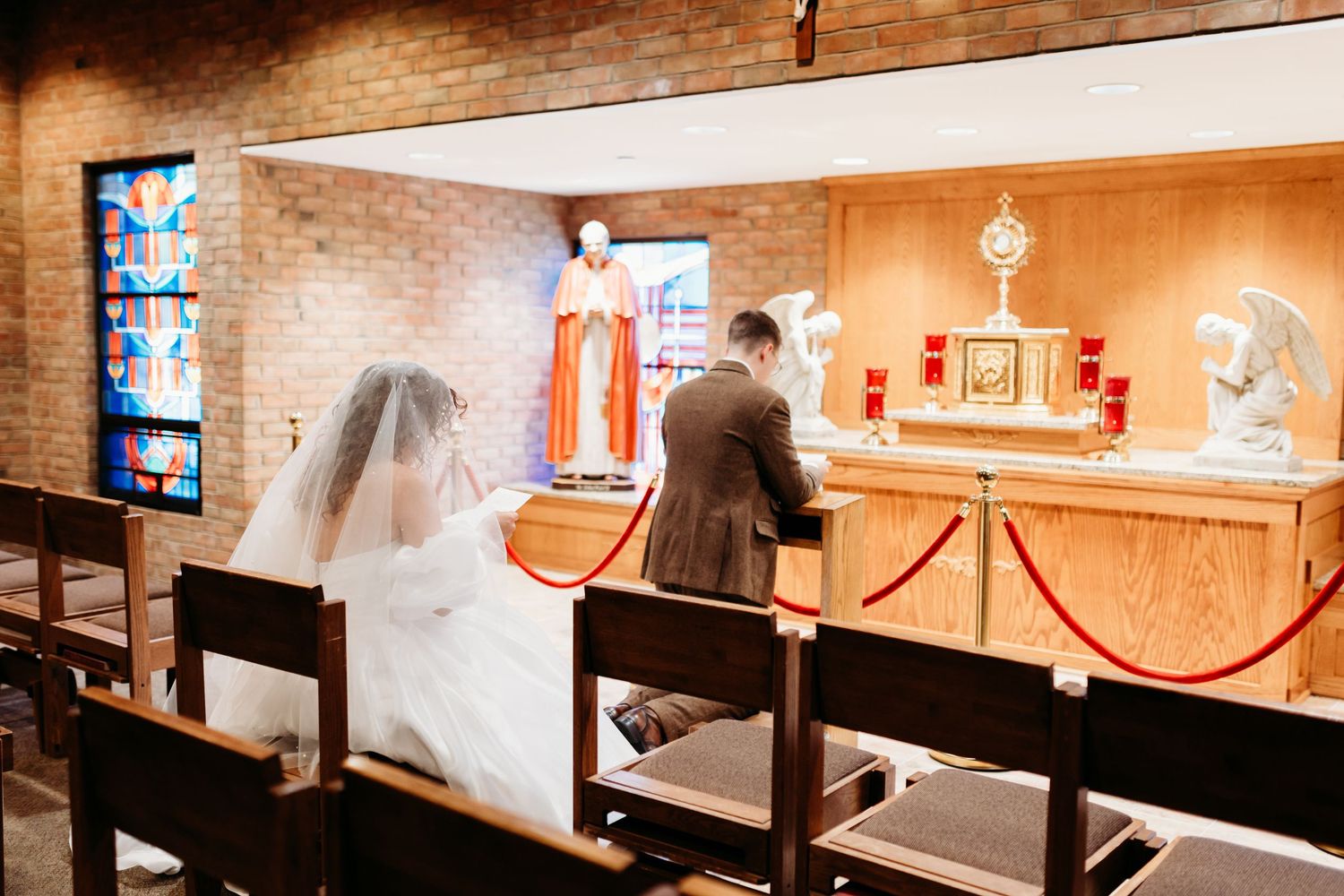 A Catholic couple prayer before the Blessed Sacrament in the Adoration chapel before their wedding Mass and a photographer snaps a photo.
