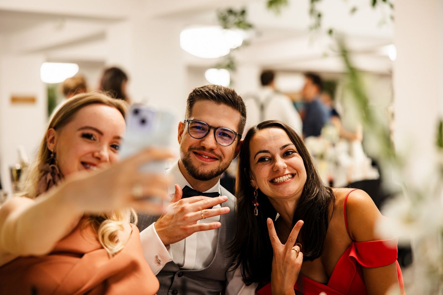 Koleżanki robiące sobie selfie telefonem z Panem młodym przy stoliku