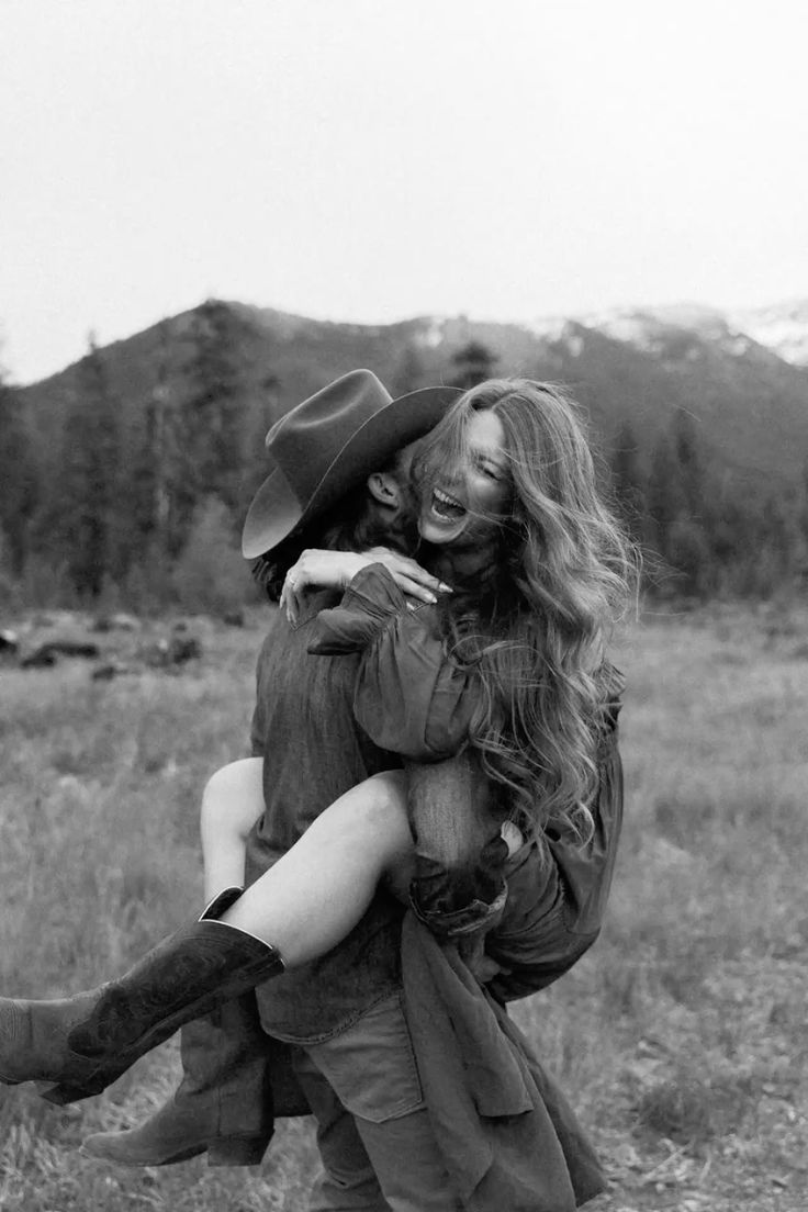Romantic western-themed couple in denim and black embrace and kiss while sitting on a fence at sunset.
