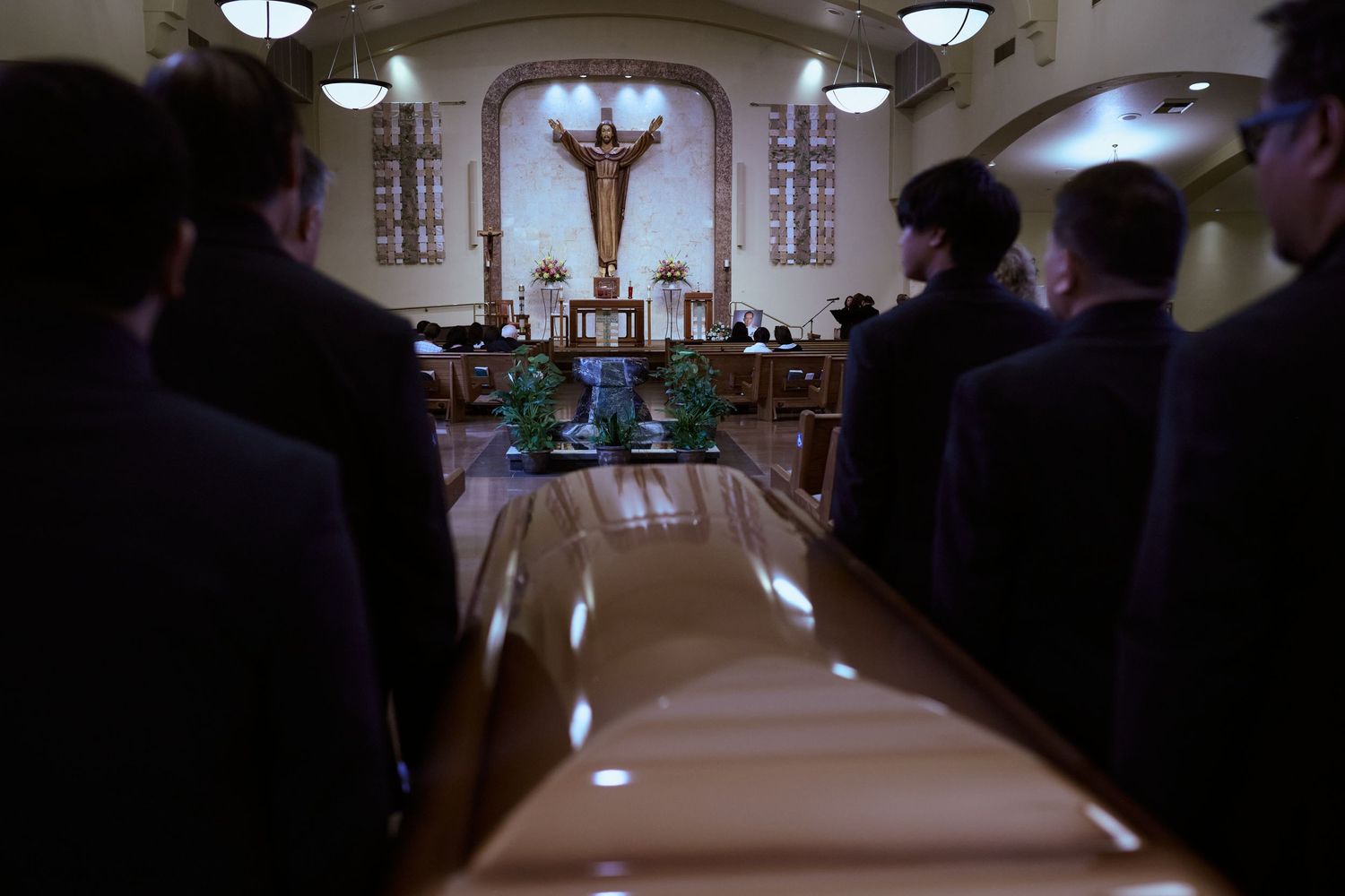 View down a church aisle during service with people sitting in pews and a crucifix mounted at the altar.