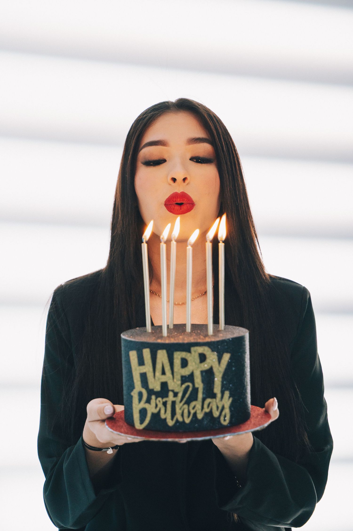 Person in black holding birthday cake with lit candles making different expressions in a photo sequence.