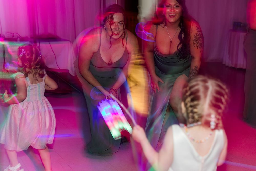 Adults enjoy a dance party with pink and purple lighting while moving and socializing on a dance floor.