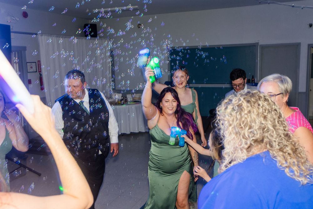 Party guests dance under bubbles and colorful lights at an indoor celebration event.