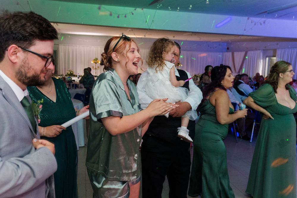 Party attendees socializing and dancing under blue and green ambient lighting at an indoor venue.