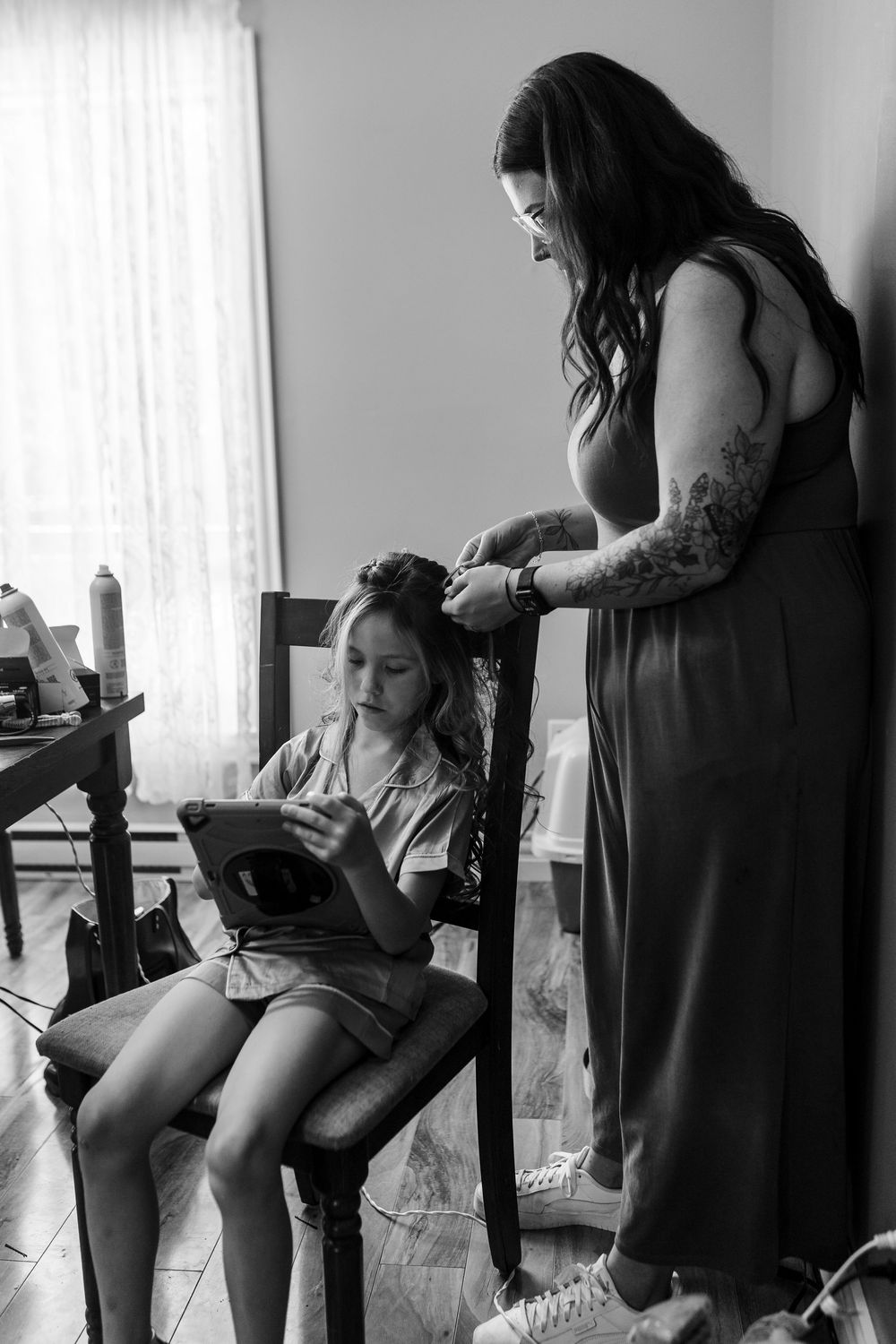 Black and white image of a hairstyling session with someone reading a tablet while getting their hair done.