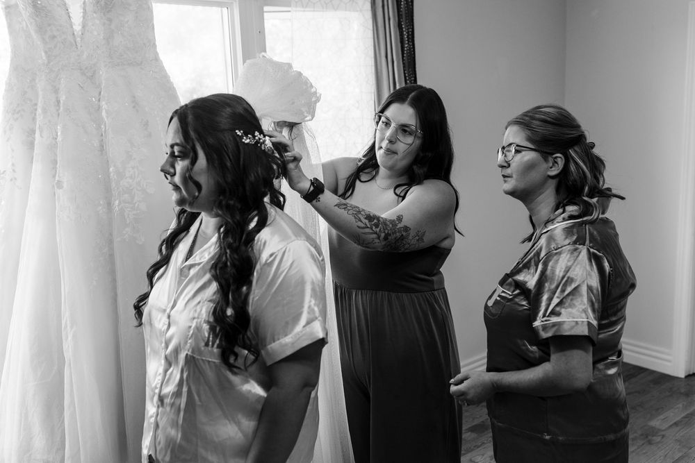 A black and white candid photograph shows a group preparing for a wedding in a brightly lit dressing area.