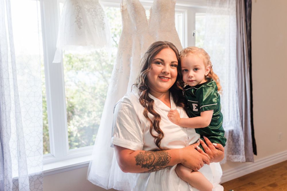 A parent and child share an intimate moment near large windows in a bright sunlit room.