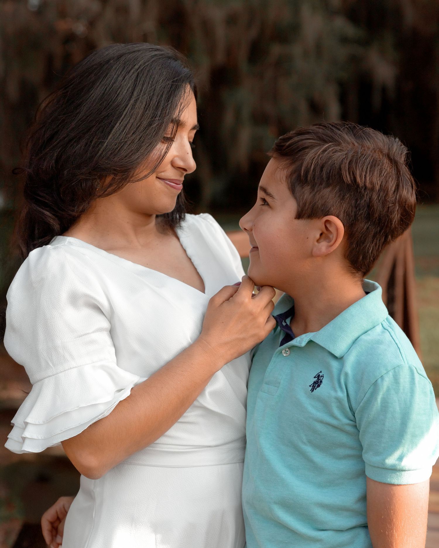 A caring moment shared between two people wearing white and turquoise outfits against a natural background.