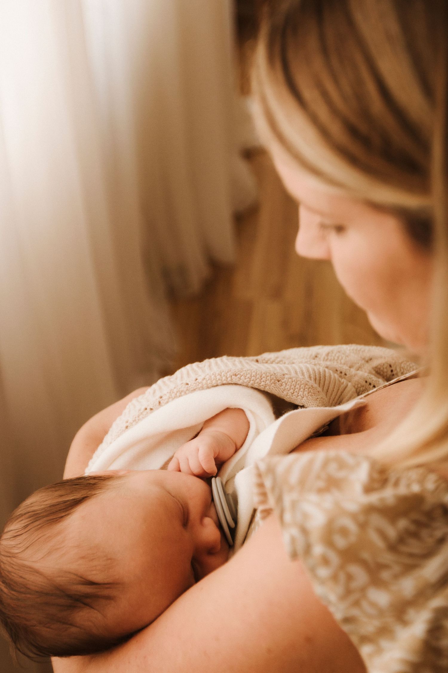 Intimate nursing moment captured in soft natural light with gentle tones and tender expressions.