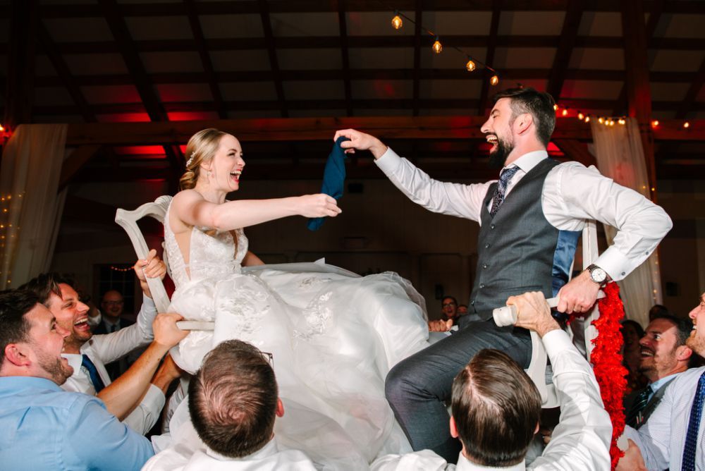 Wedding celebration with couple being lifted by guests during a lively dance reception.